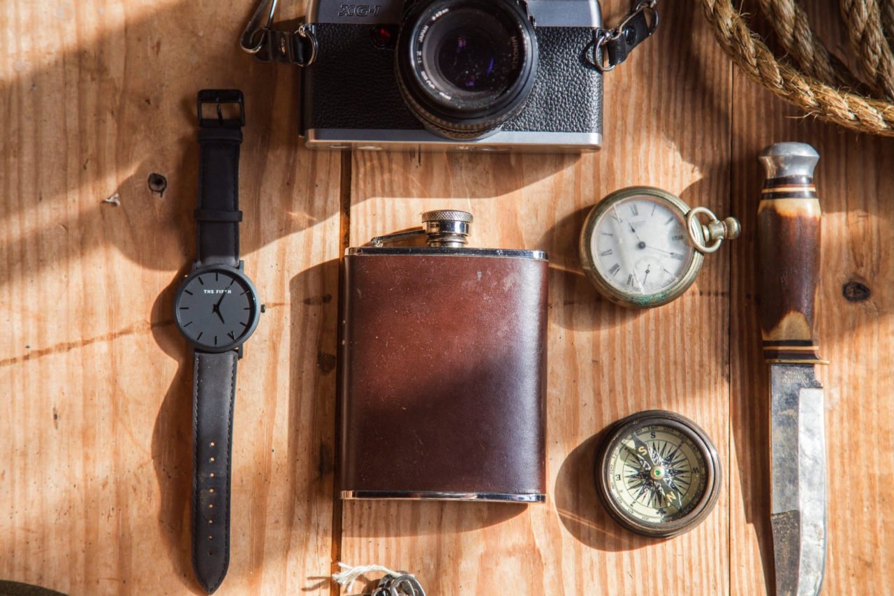 wooden table with flask, watch, camera, knife