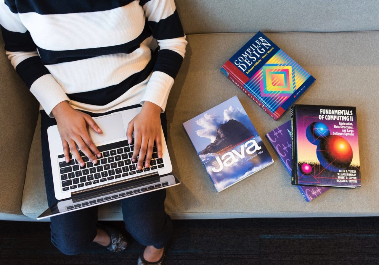 sitting on bench with promgramming books using laptop